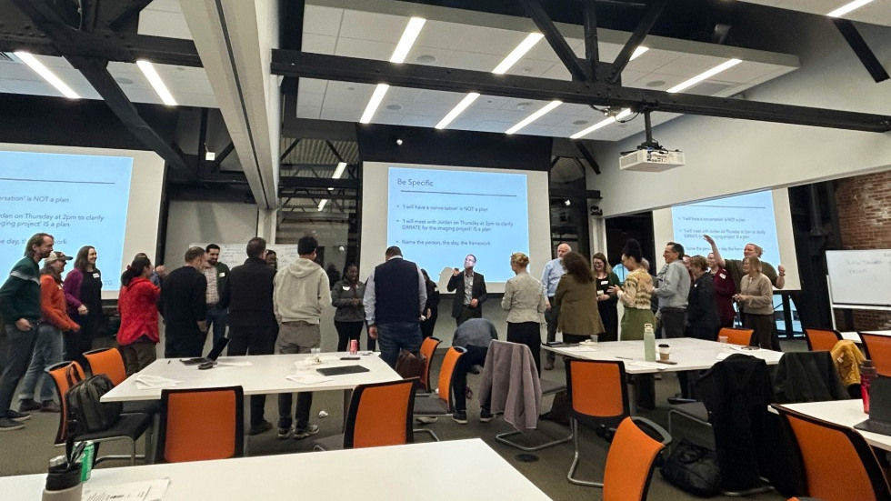 Faculty gather at the front of the room after the presentation to discuss among themselves