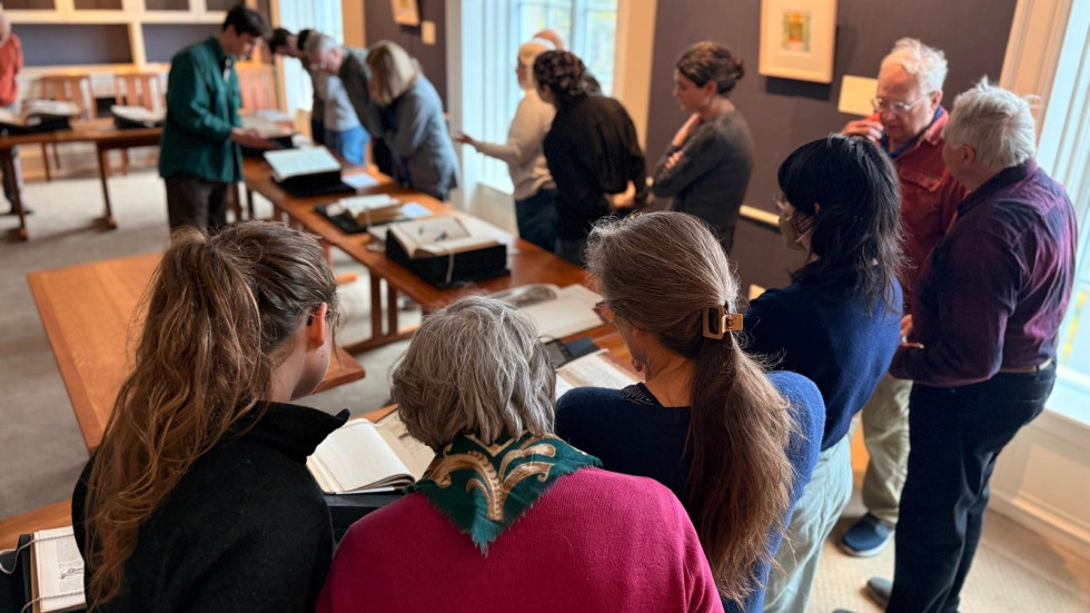 People examine ornithological archives around a library table.