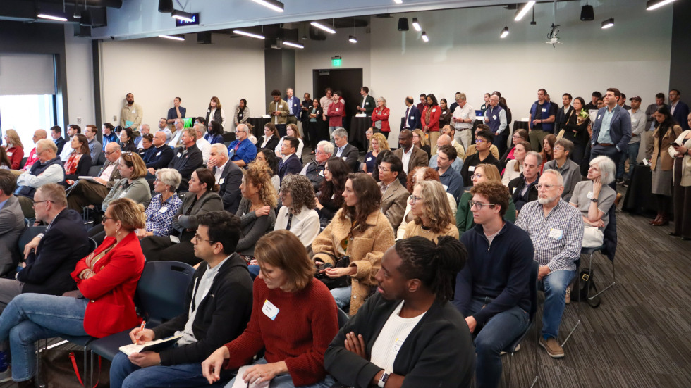 A full crowd seated in rows and standing at the back of the room.
